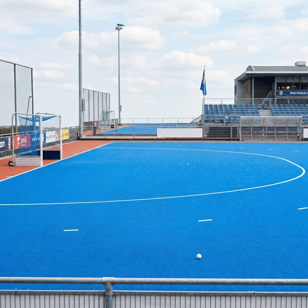 Field hockey players competing on a blue outdoor pitch before spectators